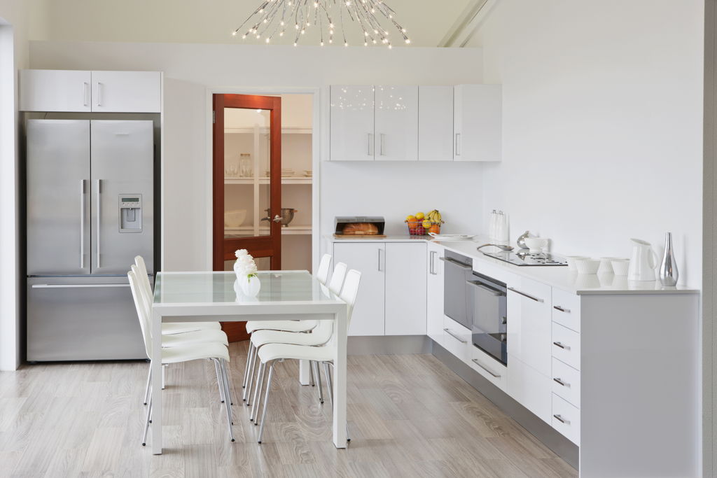 White kitchen with wooden floor, silver fridge, white kitchen cabinets, stove, glass dining table and white chairs