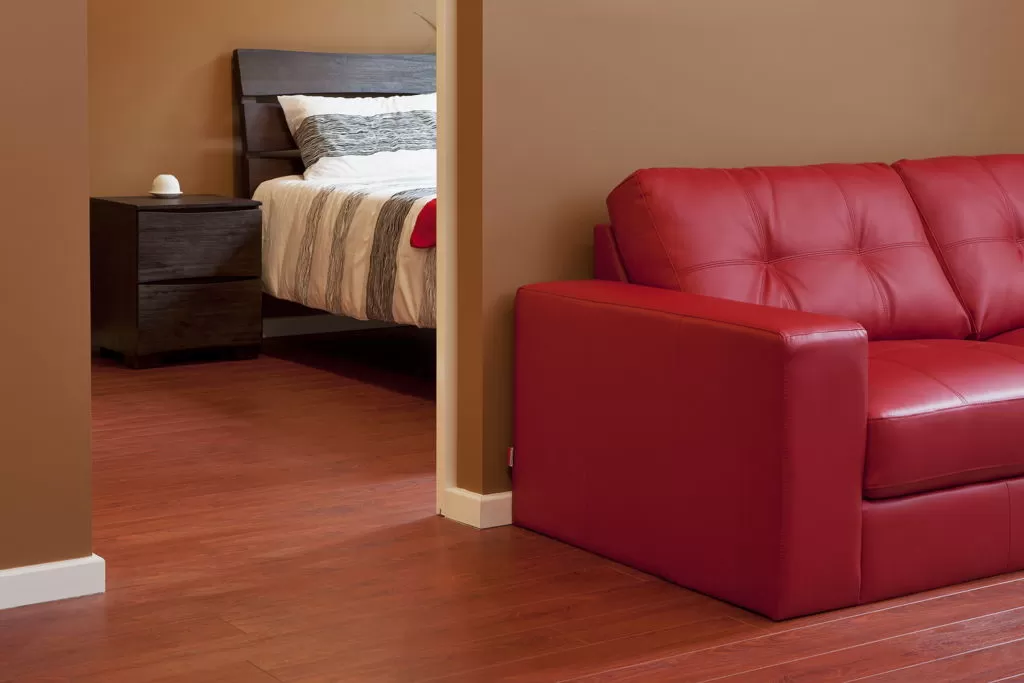 Doorway to bedroom showing bed and night stand in the background and red living room couch in the foreground