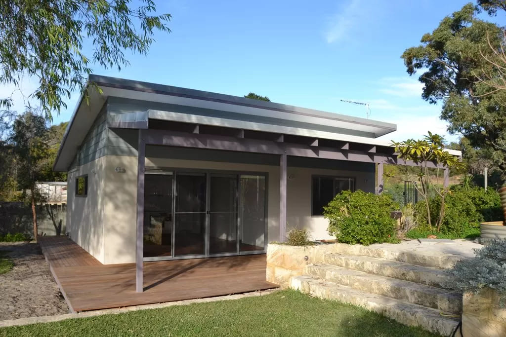 Front of granny flat with stone steps, lawn, wooden deck, awning and sliding glass doors 