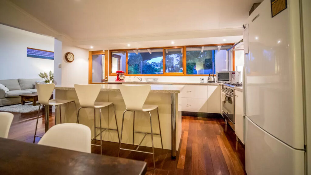 Kitchen with wooden floor, white refrigerator, white marble counter and white kitchen stools. 