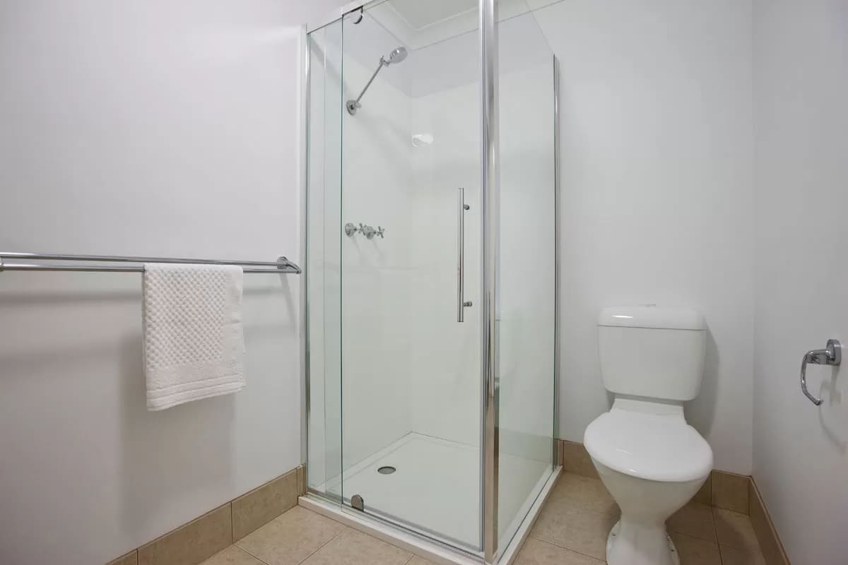 Bathroom with glass shower, towel rack and toilet on beige tiles 