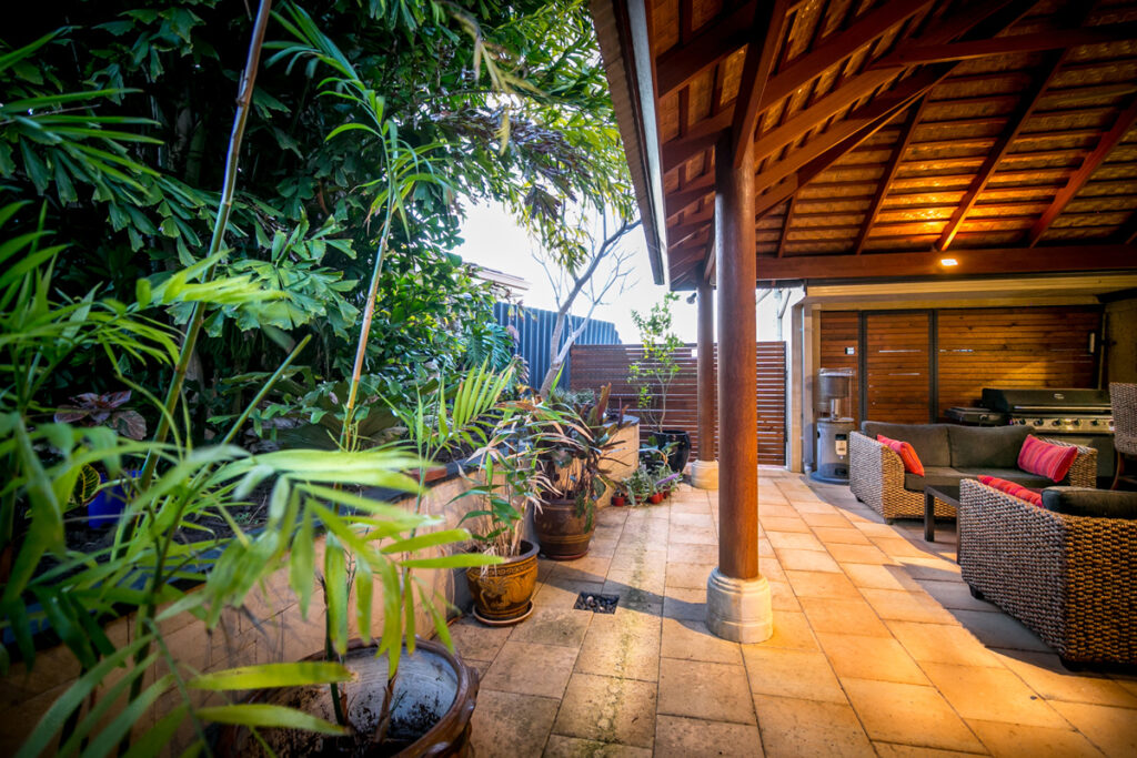 Back of house with an array of plants and wooder shelter on stone tiling