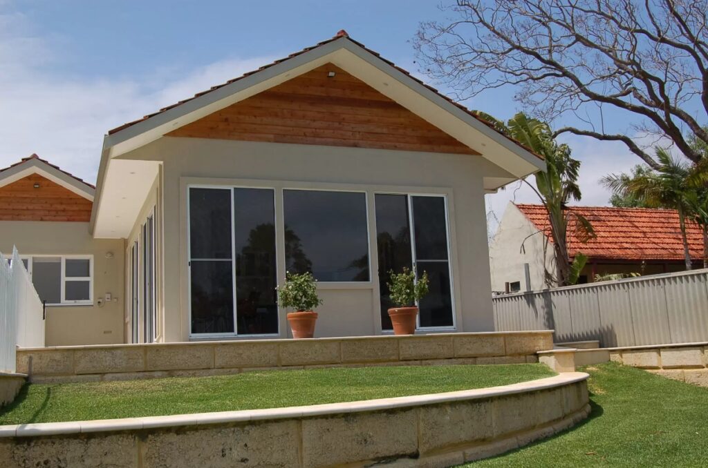 A small house with a sliding glass door, two potted plants and a lawn in front of it