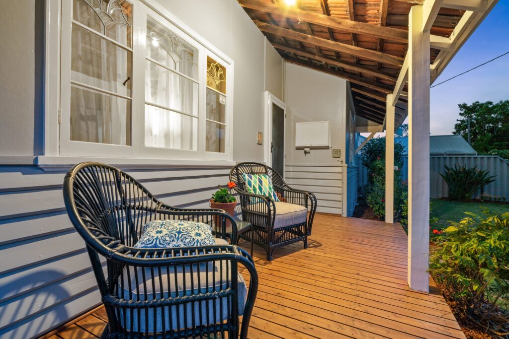grey house with a deck and two wicker chairs sitting on the deck with a potted plat between them
