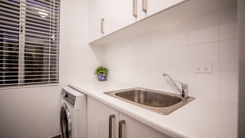 Sink with cabinets above and below, with washing machine below and blinds on the window