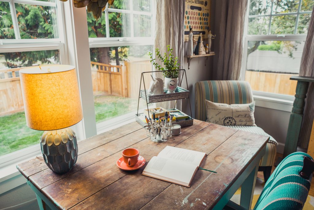 book sitting on wooden table with teacup, lamp and plants, overlooking a backyard outside